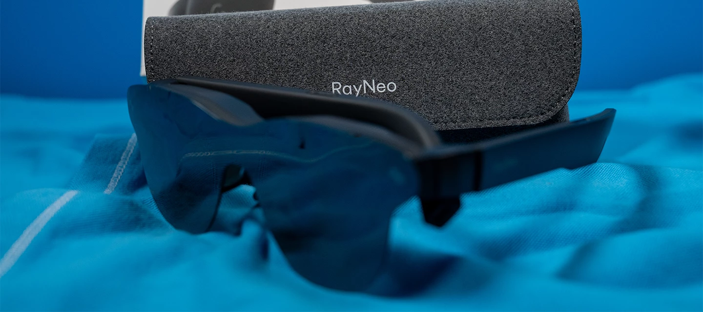 Auf einer blauen Decke liegt im Vordergrund die RayNeo Air 3s Pro. Im Hintergrund das das Brillenetui zu sehen.
