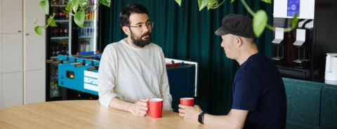 Two people discussing over cups of coffee in a colorful office space.