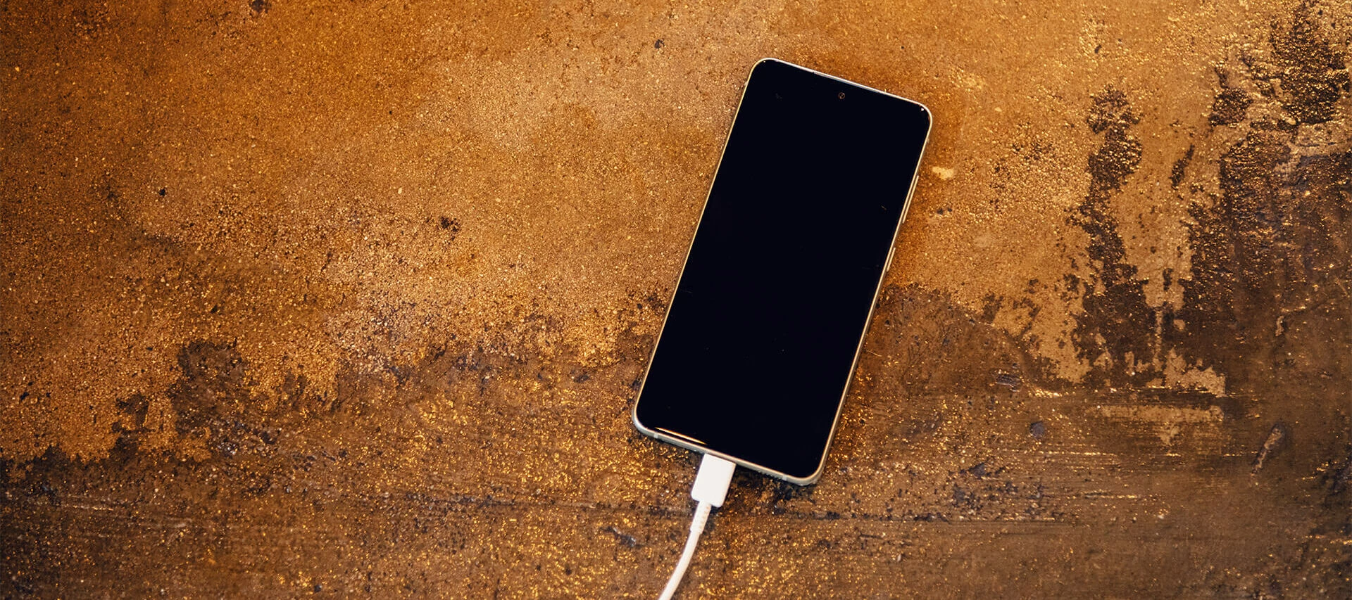 En mobiltelefon ligger på en betongyta och laddas med en vit USB-kabel.