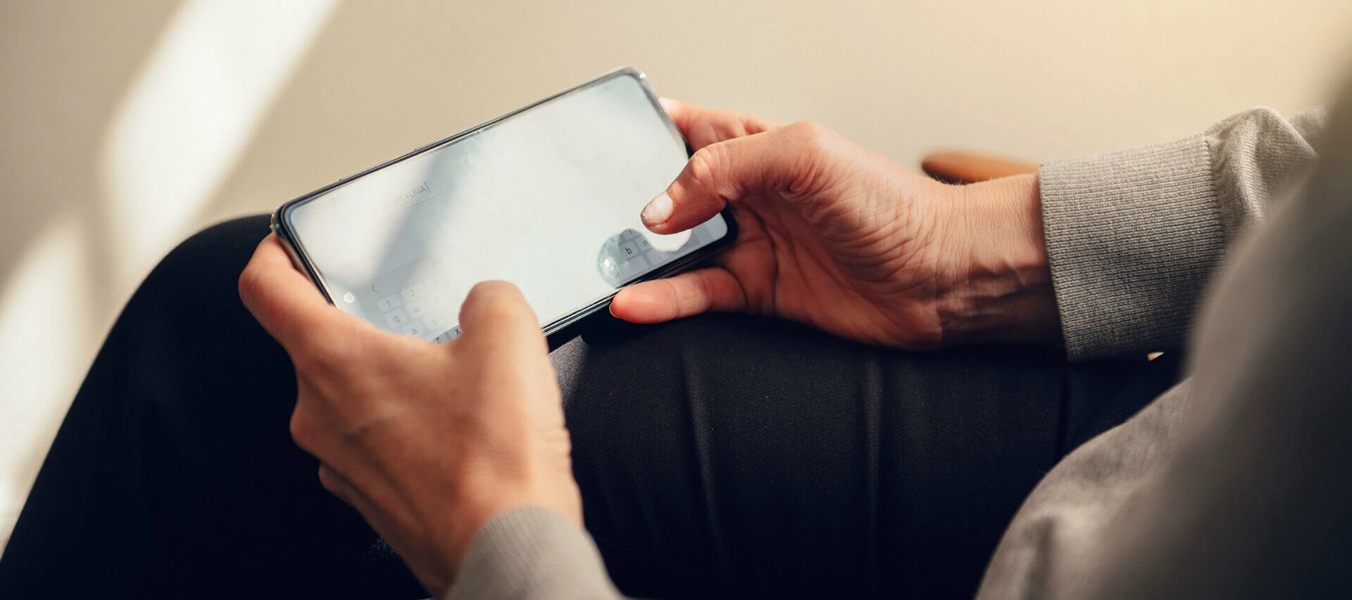 Närbild av händer som håller en smartphone och använder den, med suddig bakgrund.