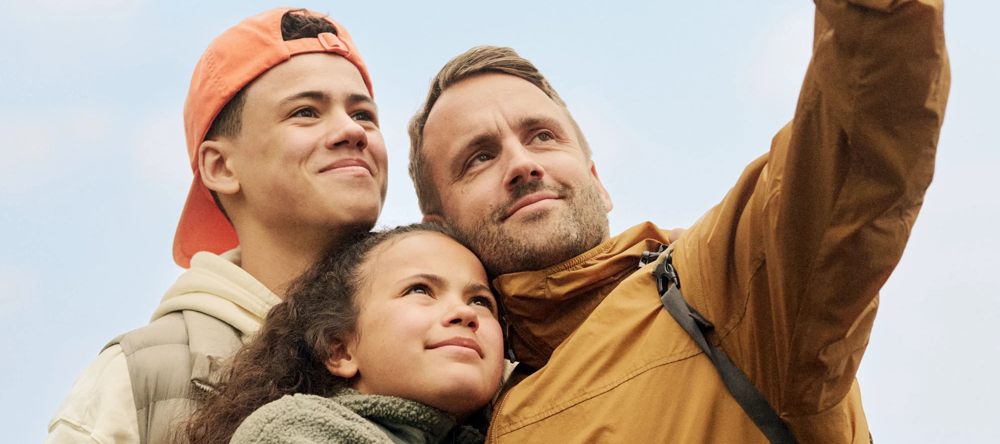 En familj på tre personer står och tar en selfie utomhus.