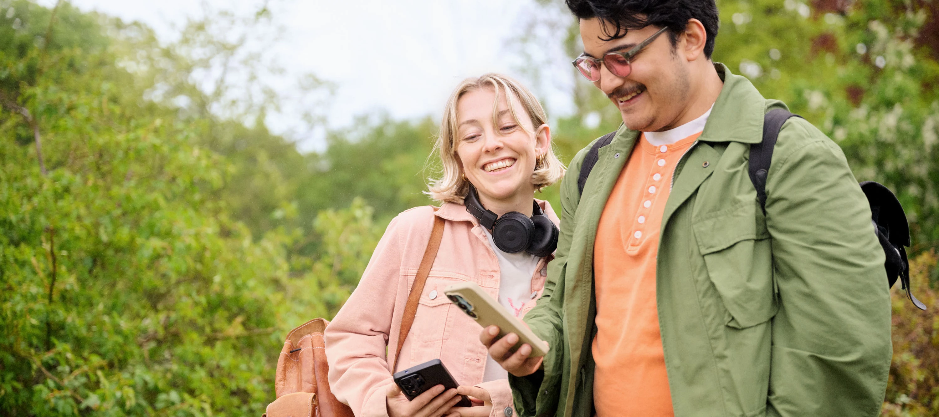 Två personer använder sina mobiler ute i naturen.